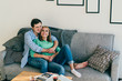 © GalakticDreamer - Lovely smiling happy cheerful couple in casual clothes chilling and cuddling on soft cozy sofa in bright modern living room