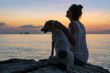 A Young Happy Woman With A Dog Watching The Sunset On The Beach