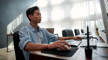 Wall Mural - designer at work. serious young asian man in casual wear working with computer while sitting at his 