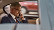 © Svitlana - I am always available. Side view of cheerful mature man in classic wear sitting in the car and talking by the phone with client
