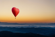 Red Hot Air Balloon In The Shape Of A Heart Flying Over The Mountain