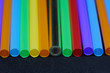 A reuseable transparent glass straw in a row of colorful plastic straw