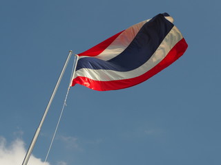 Thai flag waving on the top of pole on sunny day with clear blue sky.