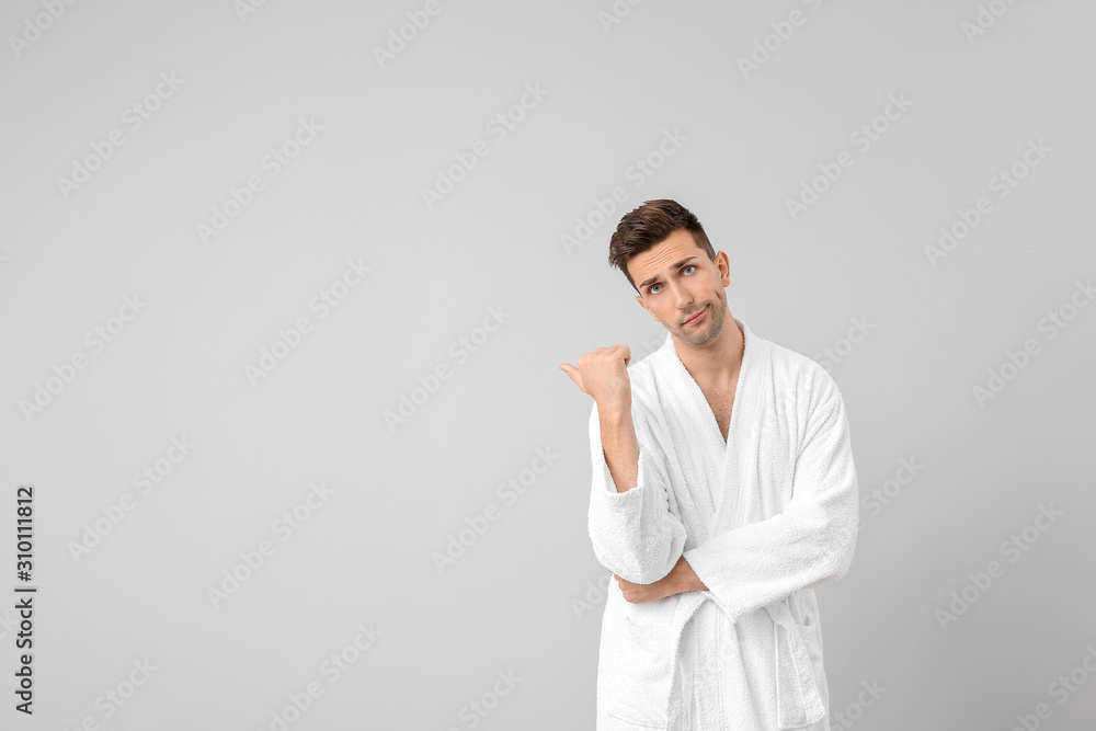 Handsome man in bathrobe pointing at something on grey background