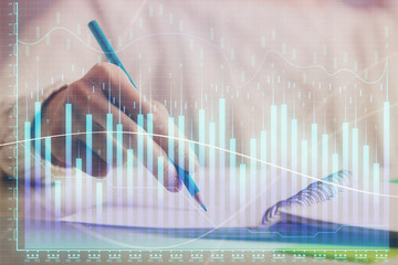 Financial forex graph displayed on hands taking notes background. Concept of research. Double exposure