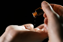 Skin Care And Treatment - Woman Pouring Oil In A Hand From Vial On Black Background