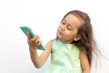 little girl with a smile looks at the camera phone isolated on a white background.  Charming kid makes selfie on the phone. The concept of modern children and fashion on gadgets