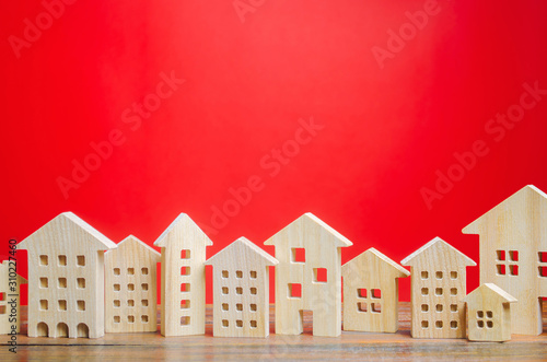 Miniature wooden houses on a red background. Real estate concept. City. Agglomeration and urbanization. Market Analytics. Demand for housing. Rising and falling home prices. Population. Copy space