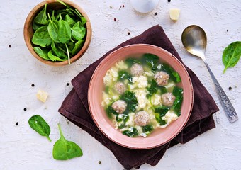 Homemade Italian wedding soup with meatballs, fresh spinach, egg and parmesan cheese in a clay bowl on a light concrete background. Spinach recipes. Italian food.