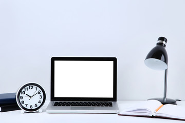 Laptop computer with notepad, round clock and electrical lamp on grey background