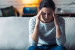 © nenetus - Young woman with headache sitting on the sofa in the living room at home.