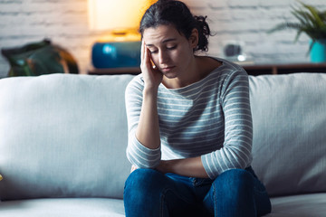 Wall Mural - Worried young woman thinking while sitting on sofa in the living room at home.