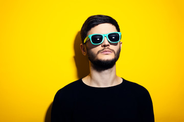  Studio portrait of young serious man wearing cyan sunglasses and black sweater on yellow background.