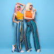 © evgenij918 - Two fashionable girl posing in Studio. Beautiful Adorable young woman in Stylish summer colorful outfit, Trendy dyed hair, make up. Glamour model sister friend, fashion concept on blue, full-length