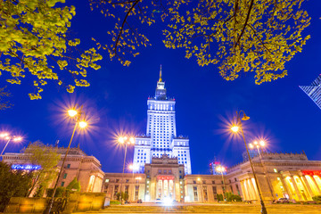 Palace of Culture and Science in downtown Warsaw, Poland at night. Historical art deco building from the Soviet era at dusk, under clear blue sky.