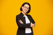 © Brastock Images - Attractive middle aged woman with beautiful smile on yellow wall. Pretty older business woman, successful confidence with arms crossed.