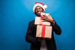 © F8  \ Suport Ukraine - Young African American man wearing a santa hat offering a gifts on blue background