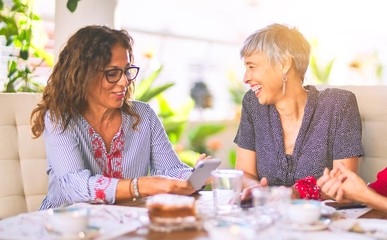 Wall Mural - Meeting of middle age women having lunch and drinking coffee. Mature friends smiling happy using smartphone at home on a sunny day