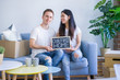 © Krakenimages.com - Young beautiful couple sitting on the sofa holding blackboard with message at new home around cardboard boxes