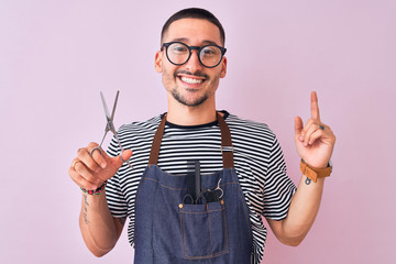 Sticker - Young handsome hairdresser man wearing apron over pink isolated background very happy pointing with hand and finger to the side