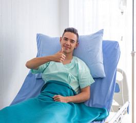 Portrait of asian young man patient lying in a hospital bed and a thumb up with nice smile confident in the treatment process of the hospital. Health and Personal Accident Insurance concept.