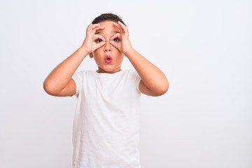 Wall Mural - Beautiful kid boy wearing casual t-shirt standing over isolated white background doing ok gesture like binoculars sticking tongue out, eyes looking through fingers. Crazy expression.