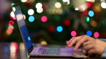 Wall Mural - Woman making online payment for holiday gifts, Christmas tree lights on background, 4k