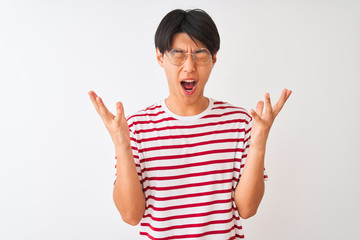 Young chinese man wearing glasses and striped t-shirt standing over isolated white background celebrating mad and crazy for success with arms raised and closed eyes screaming excited. Winner concept