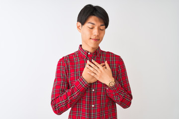 Wall Mural - Young chinese man wearing casual red shirt standing over isolated white background smiling with hands on chest with closed eyes and grateful gesture on face. Health concept.