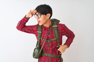 Wall Mural - Chinese hiker man wearing backpack canteen glasses over isolated white background very happy and smiling looking far away with hand over head. Searching concept.