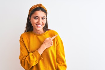 Wall Mural - Young beautiful woman wearing yellow sweater and diadem over isolated white background cheerful with a smile of face pointing with hand and finger up to the side with happy and natural expression