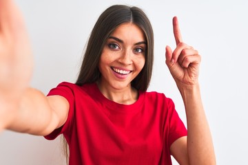 Wall Mural - Beautiful woman wearing red t-shirt make selfie by camera over isolated white background surprised with an idea or question pointing finger with happy face, number one