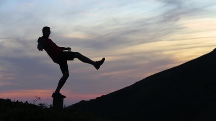 Wall Mural - Dark silhouette of a hiker balancing on a stone in evening mountains.