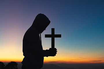 Silhouette human praying and holding christian cross for worshipping God at sunset background.Christian, Christianity,