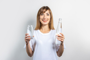 Young woman holds a bottle and a glass with clear water on a light background. Banner. Concept of thirst, heat, health and beauty care, water balance