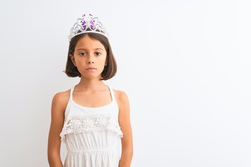 Sticker - Beautiful child girl wearing princess crown standing over isolated white background Relaxed with serious expression on face. Simple and natural looking at the camera.