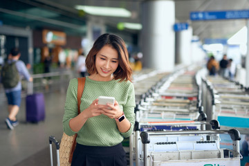 Young Asian woman waiting on the side of the street for her ride that she booked via a ride-hailing app.