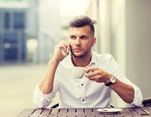 business, technology, communication and people concept - young man drinking coffee and calling on smartphone at city street cafe