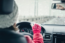 Woman in the red jacket, hat and christmas gloves is driving on the highway at the winter snowfall.  View from the back seat of the car. concept.