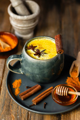 Golden milk in grey mug, turmeric latte made with curcuma, cinnamon, anise, honey. Healthy hot winter drink, natural, organic beverage. Close up, front view.  Wooden rustic background