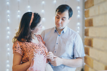 loving couple embracing and tockings considers children's clothes. Healthy lifestyle concept, IVF fashion for pregnant women, children. A man and a woman look into each other's eyes. Husband hugs preg