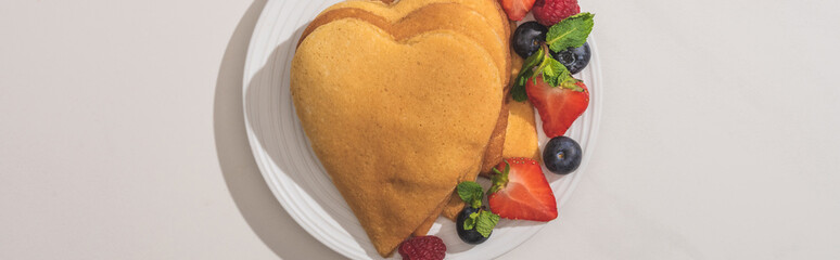 Wall Mural - top view of heart shaped pancakes with tasty berries on plate on white background, panoramic shot