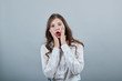 © Petro - Shocked caucasian young woman in fashion white shirt holding hands on cheek with opened mouth, looking at camera isolated on gray background in studio. People sincere emotions, lifestyle concept.