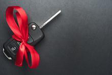 Car Key With Red Bow On Dark Black Slate Plate Background. Christmas Or Valentine's Day Gift Or Present Abstract Concept. Copy Space On The Left. Flat Lay Top View.