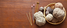 Top View Of A Wicker Basket With Balls Of Wool Yarn For Hand Knitting And A Set Of Hooks And Knitting Needles On An Old Wooden Table. Place For Text, Banner. Flat Lay, Close Up, Copy Space, Mock Up