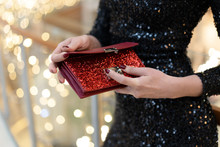 Red Little Female Clutch Bag With Sequins. Brilliant, Festive For A Party. Girl In A Black Dress Holds In Her Hands. Accessories For A Female Image