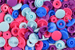 Top view of bunch of colorful blue, purple and pink plastic snap fastener buttons