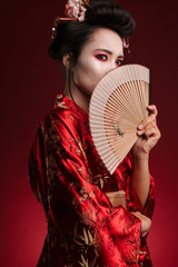 Wall Mural - Image of young geisha woman in japanese kimono holding wooden hand fan