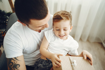 Cheerful father and son sitting near Christmas decorations. The boy is sitting with joy