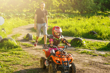 Father and daughter playing on the road at the day time. They driving on quad bike in the park. People having fun on the nature. Concept of friendly family.